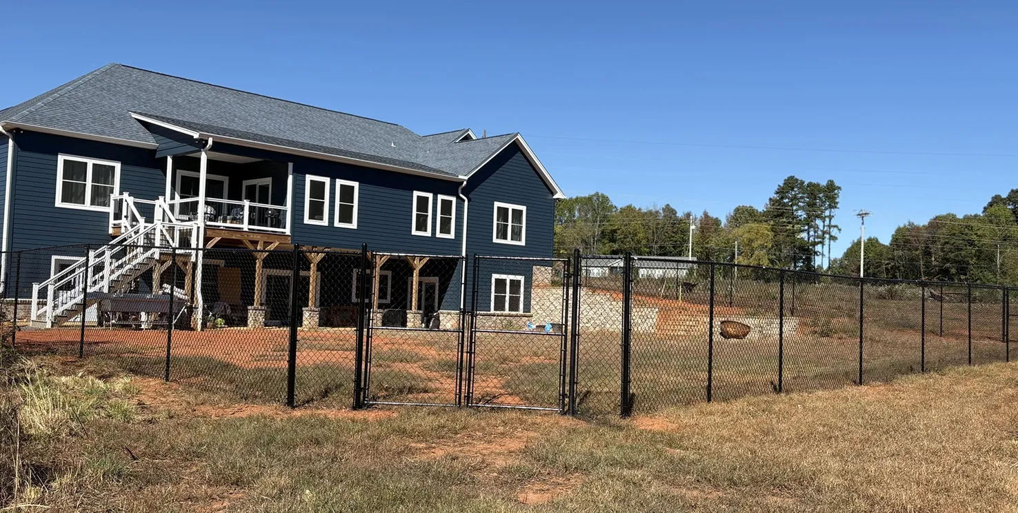 Large blue house with white trim and stairs, fenced yard with black chain-link fence and clear blue sky.