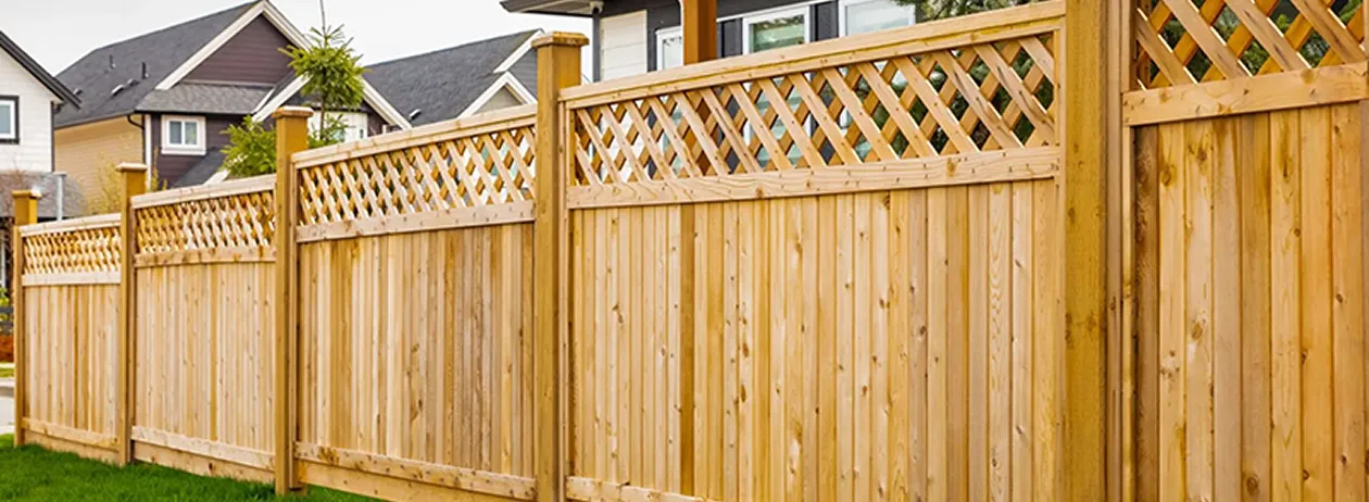 Wooden fence panels with lattice tops enclosing a suburban backyard with houses in the background.