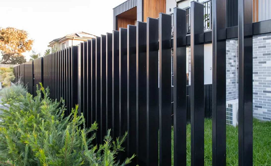 Modern black vertical metal fence along a grassy yard beside a residential building.