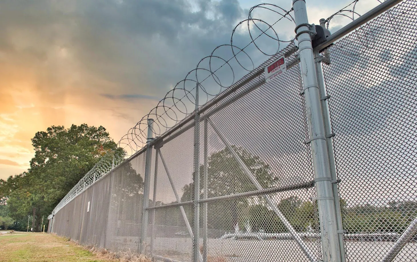 Tall chain-link commercial security fence topped with spirals of barbed wire at sunset.