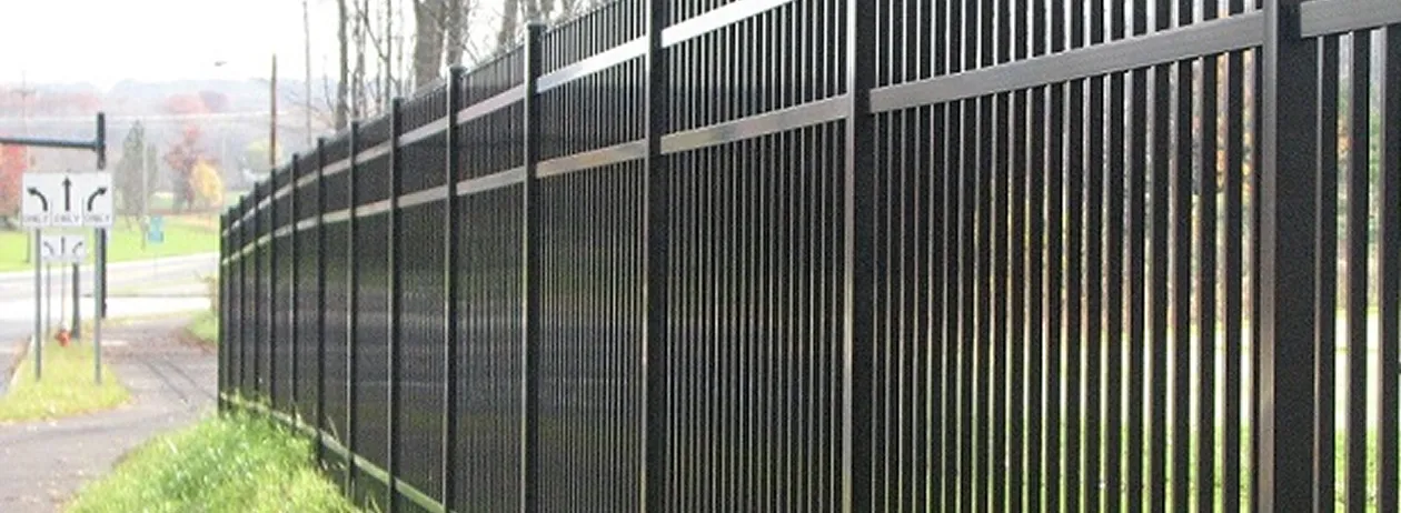 Long black metal fence with vertical bars along a roadside with traffic signs in the background.