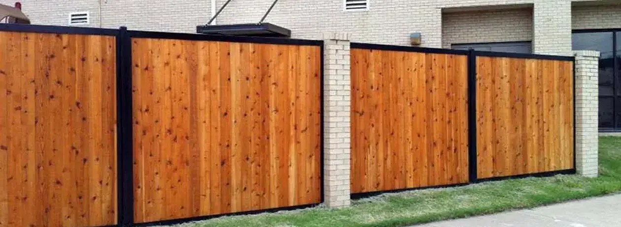 Commercial wooden fence panels with black metal frames set between beige brick pillars in front of a building.