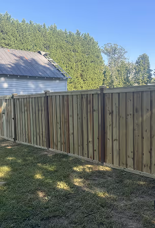 Tall wooden privacy fence with vertical panels next to a building under a clear blue sky.