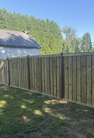 Tall wooden privacy fence with vertical panels next to a building under a clear blue sky.