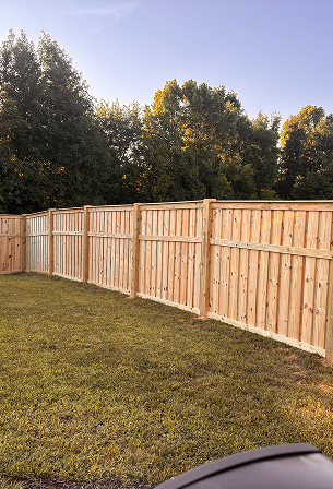 New wooden privacy fence enclosing a grassy backyard with trees in the background under a clear sky.