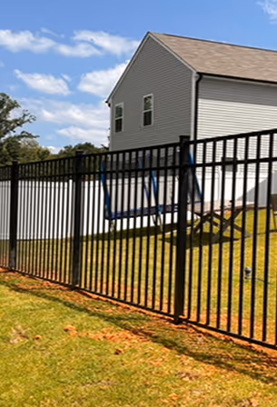 Backyard with black metal fence, blue swing, lawn chair, and a white two-story house under a cloudy sky.