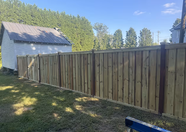 New wooden privacy fence installed next to a white shed with a metal roof in a grassy backyard.