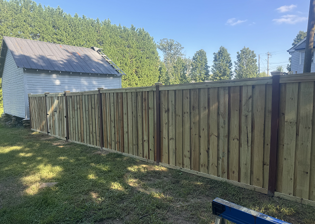 New wooden privacy fence installed next to a white shed with a metal roof in a grassy backyard.