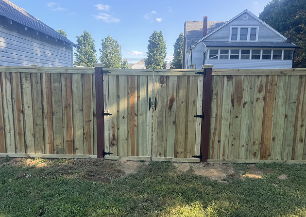 Newly installed wooden privacy fence with double gates and black metal hinges in a suburban backyard.