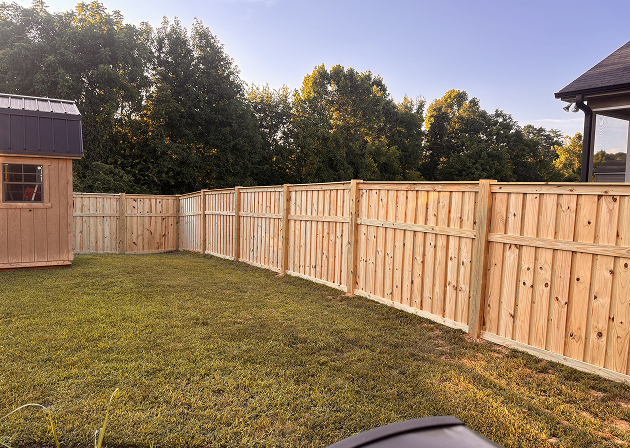 Newly installed wooden privacy fence surrounding a backyard with green grass and a small wooden shed.
