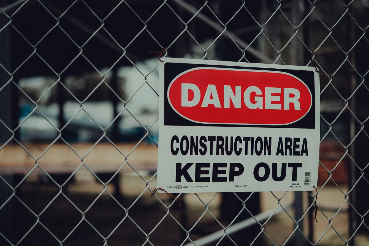 A metal chain-link fence with a sign attached that reads 'DANGER CONSTRUCTION AREA KEEP OUT' in bold letters.