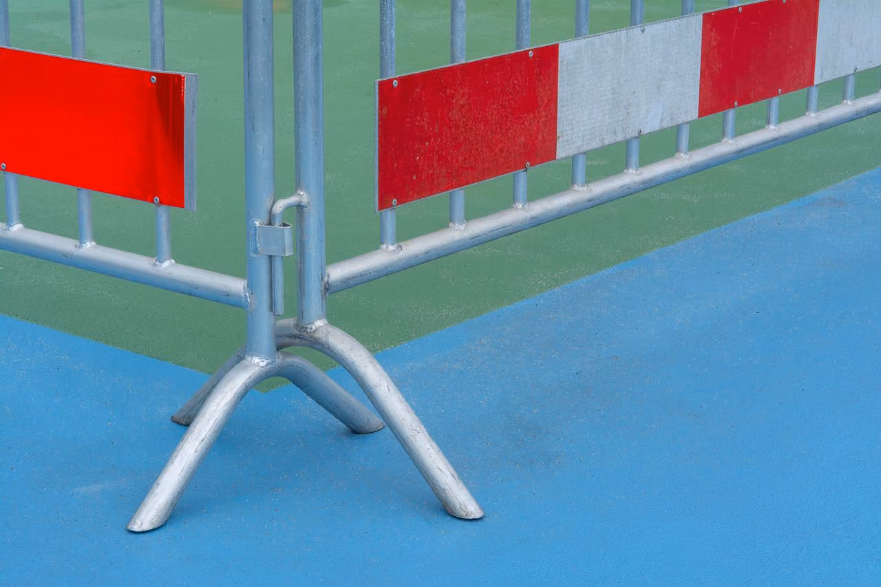 Close-up of a metal crowd control barrier with red and white reflective panels standing on a surface divided into blue and green sections.