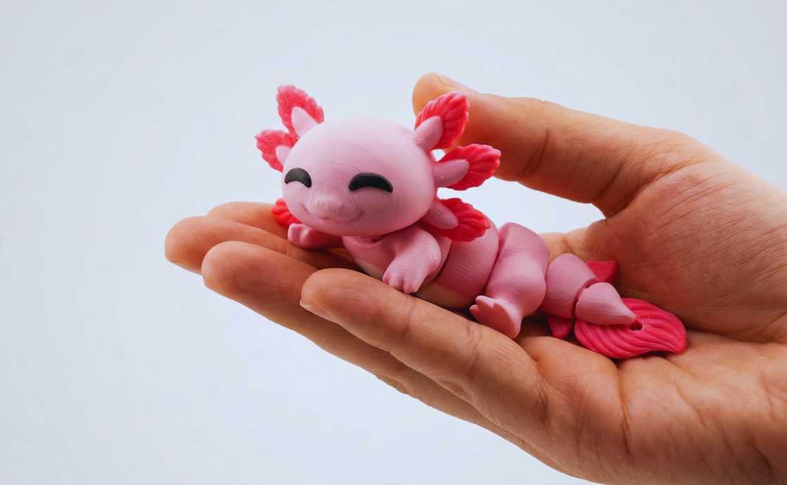 Hand holding a small pink axolotl figurine with closed eyes and red feathery gills.