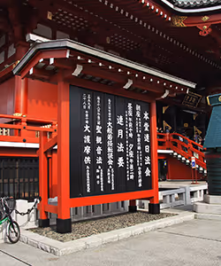 Rotes japanisches Tor mit einem schwarzen Schild, das weiße japanische Schriftzeichen zeigt.