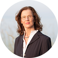 Porträt einer Frau (Christina Blake) mit Brille und braunem Anzug vor unscharfem, hellem Hintergrund.