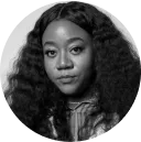 Portrait of a woman with long curly hair wearing a checkered shirt, looking directly at the camera.