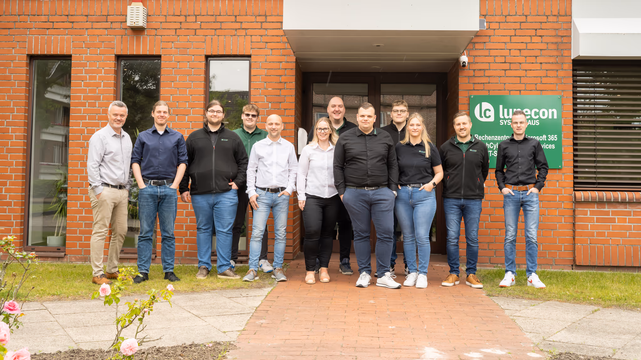 Gruppenfoto von elf Personen vor einem Backsteingebäude mit einem Schild der IT-Firma Lunecon.
