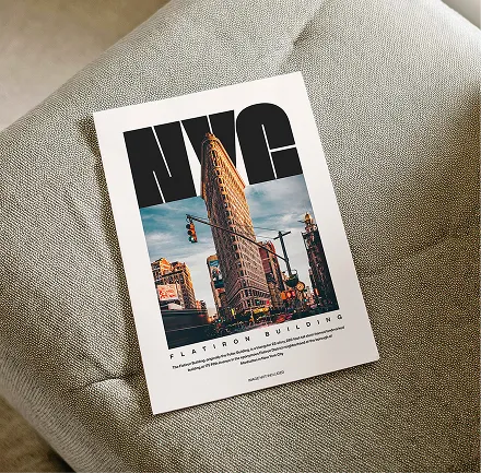 Poster of NYC Flatiron Building with large black 'NYC' text above the building image, placed on a textured gray fabric surface.