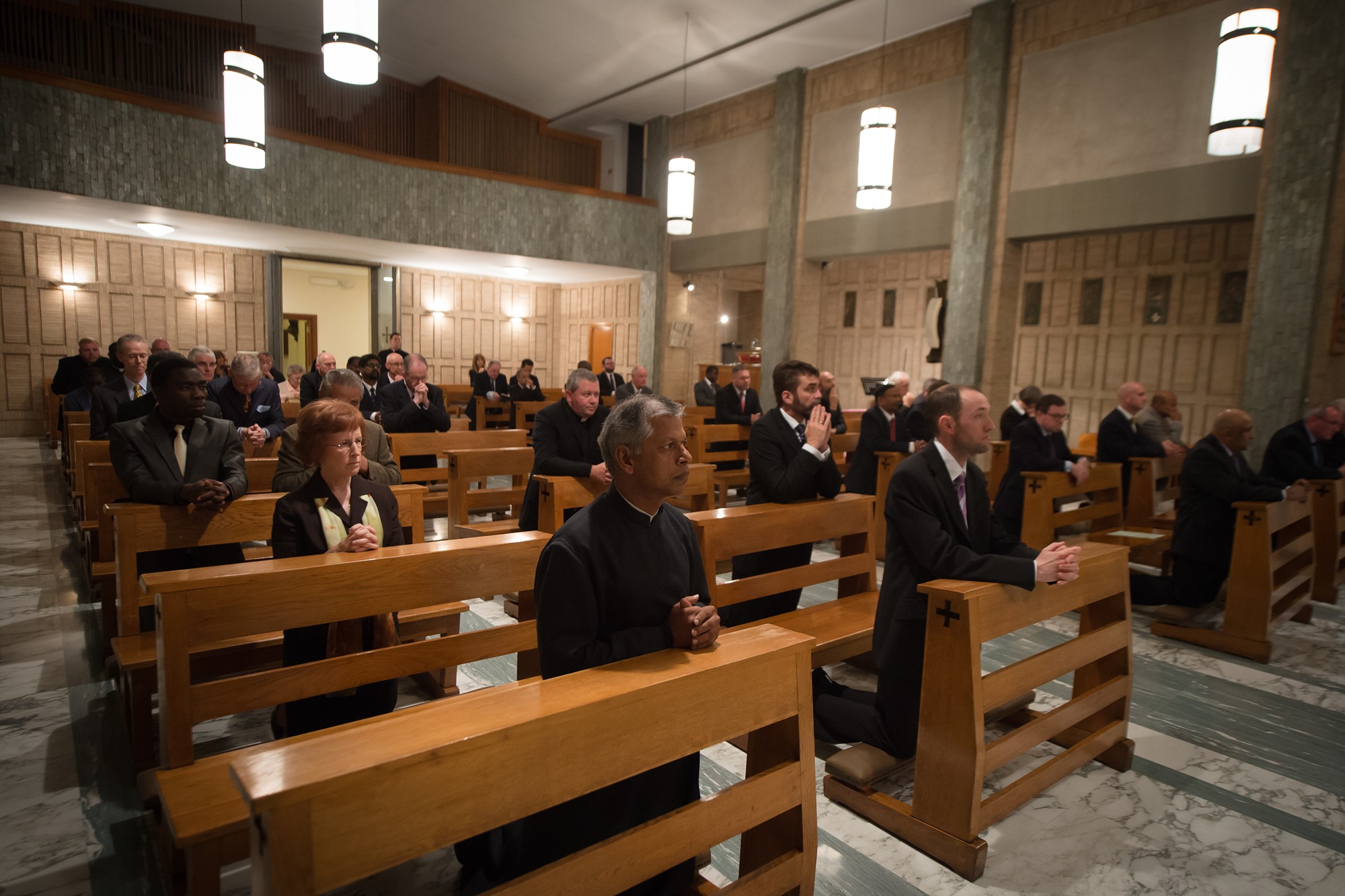 Diverse group of people kneeling and praying in wooden pews inside a church.
