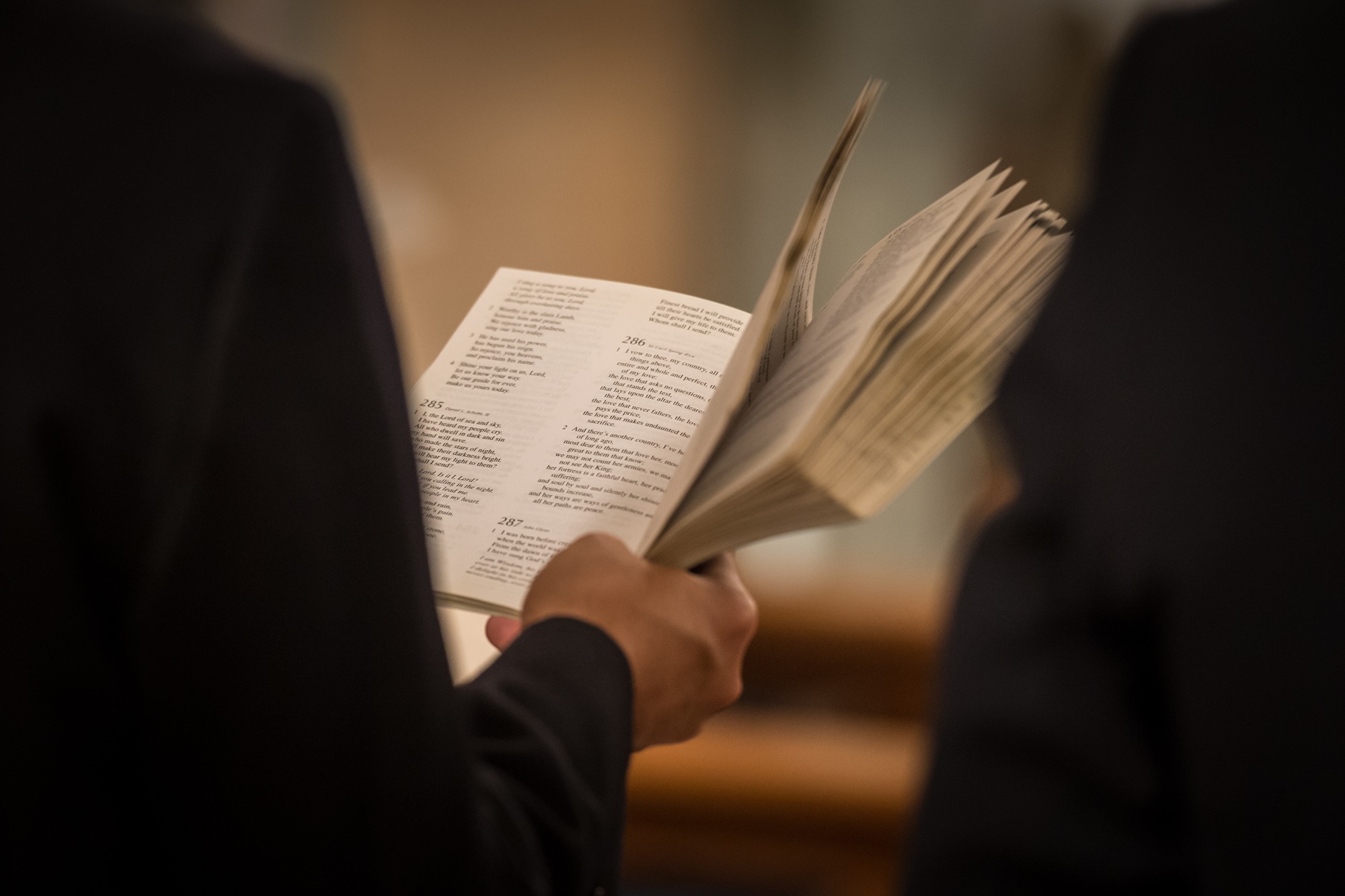 Person holding and flipping through pages of an open hymn book during a religious service.