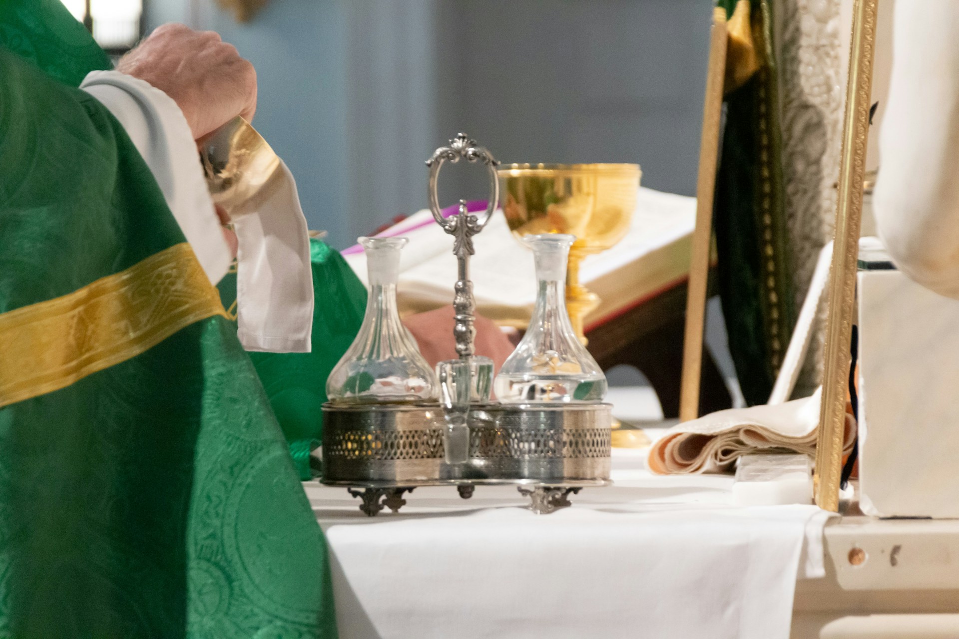 Priest wearing green vestments preparing for a Catholic mass with chalice, cruets, and altar book on the altar.