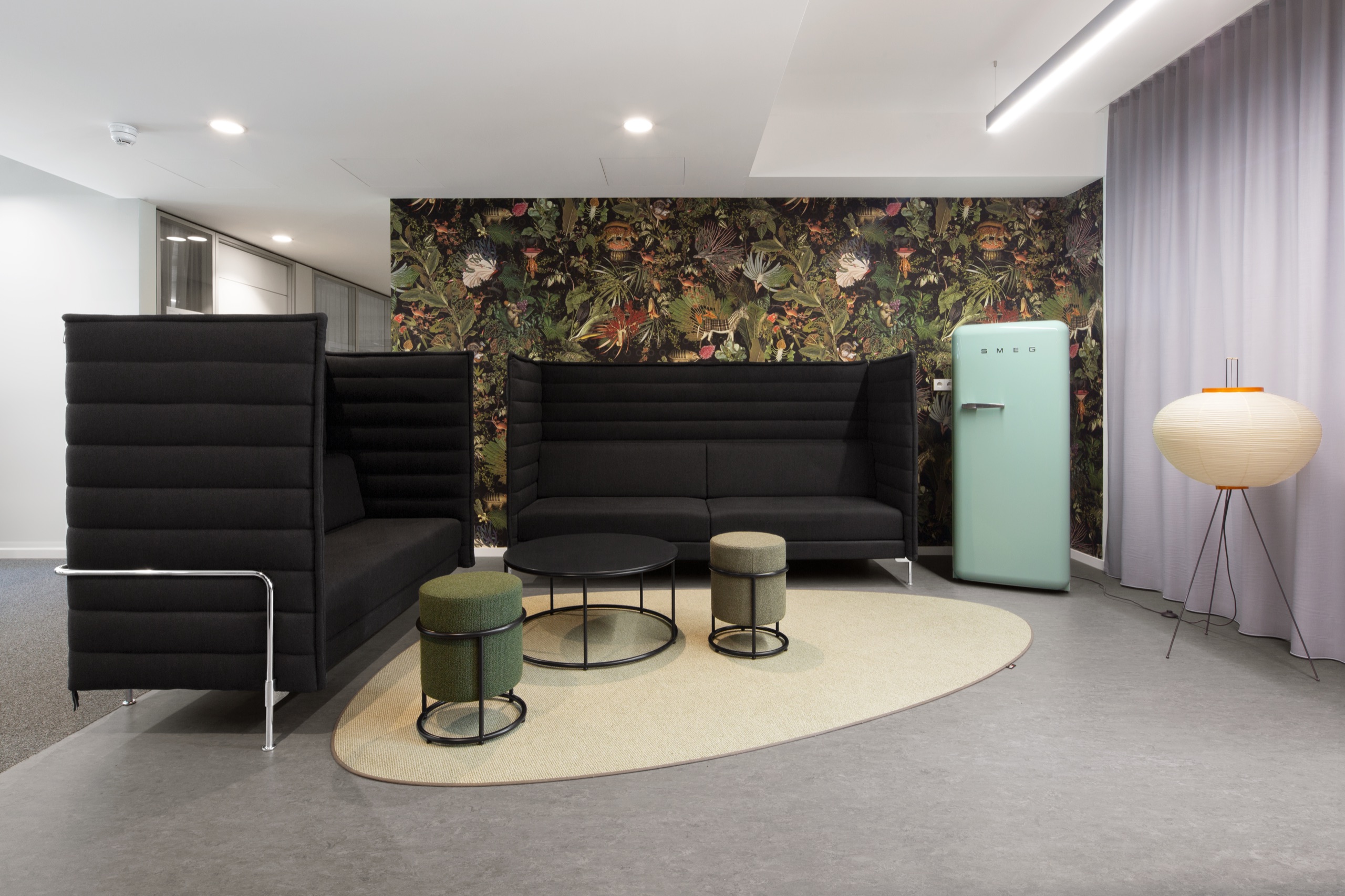 Loungezone mit schwarzen Vitra Alcove Sofas, Hockern von COR und floraler Tapete von Arte