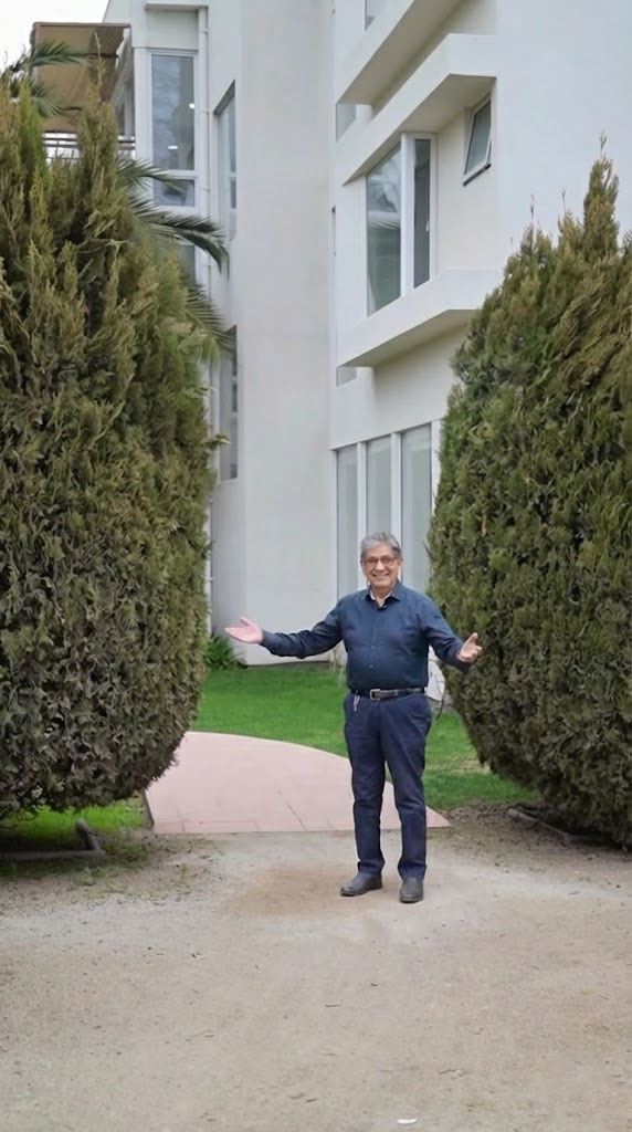 Hombre mayor y hombre adulto sonrientes abrazados al aire libre con árboles desenfocados al fondo.
