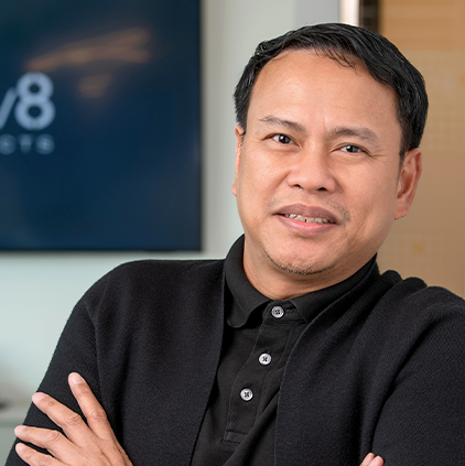 Man with short black hair wearing a black shirt and cardigan, smiling with arms crossed in an office setting.