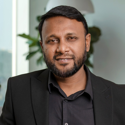Portrait of a man with a beard wearing a black suit jacket and shirt, smiling slightly in an office setting.