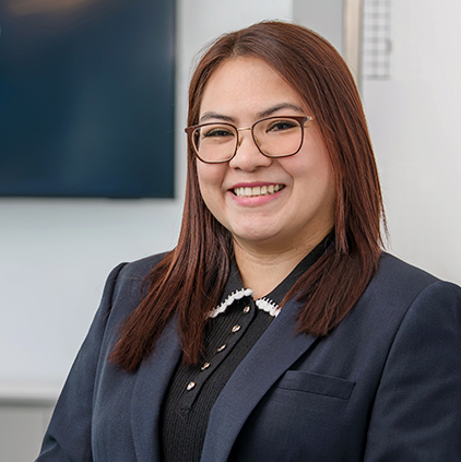 Smiling woman with straight brown hair and glasses wearing a dark blazer and black shirt in an office setting.