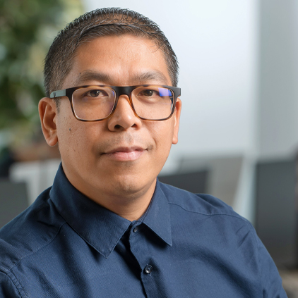 Man wearing glasses and a dark blue collared shirt looking at the camera indoors.