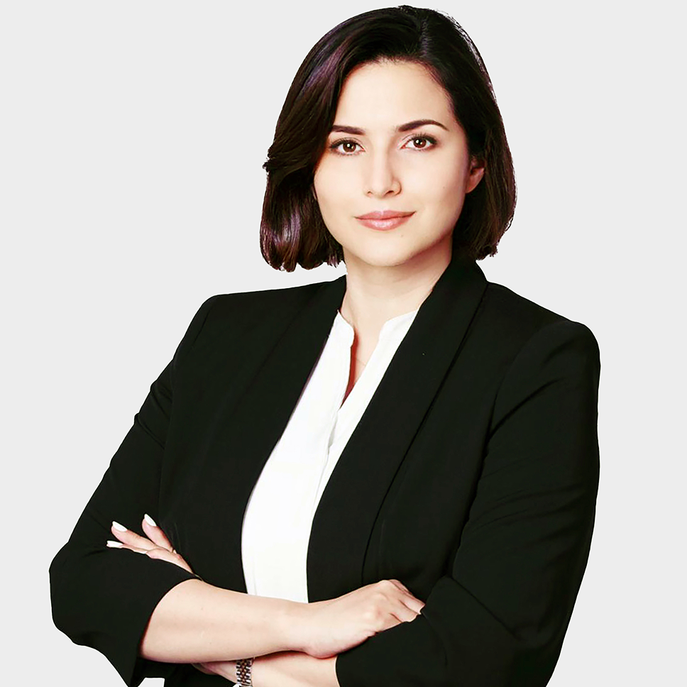 Confident woman with short dark hair wearing a black blazer and white blouse, arms crossed.