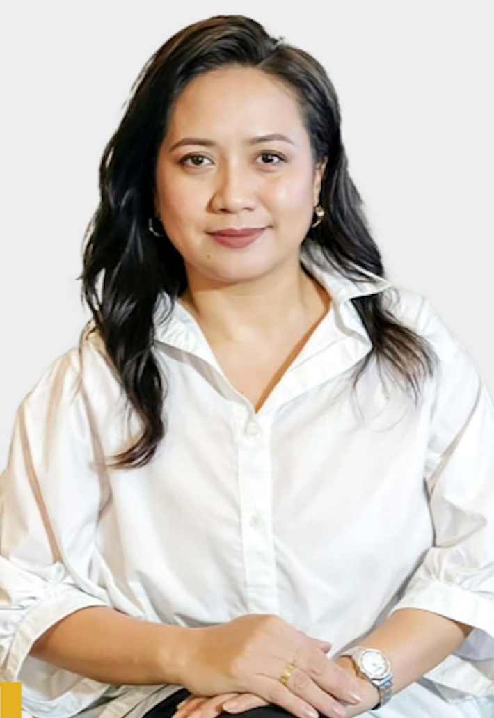 Portrait of a woman with black wavy hair wearing a white blouse, sitting with hands folded.