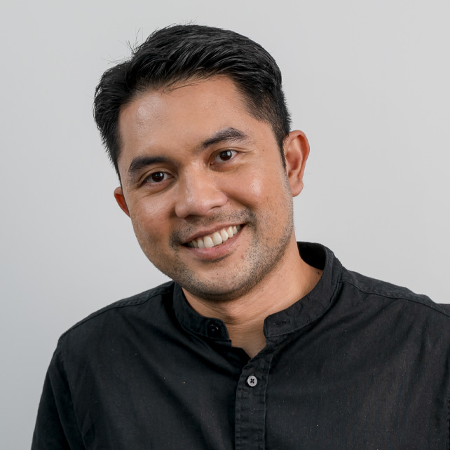 Smiling man with short black hair and trimmed beard wearing a black button-up shirt against a light gray background.