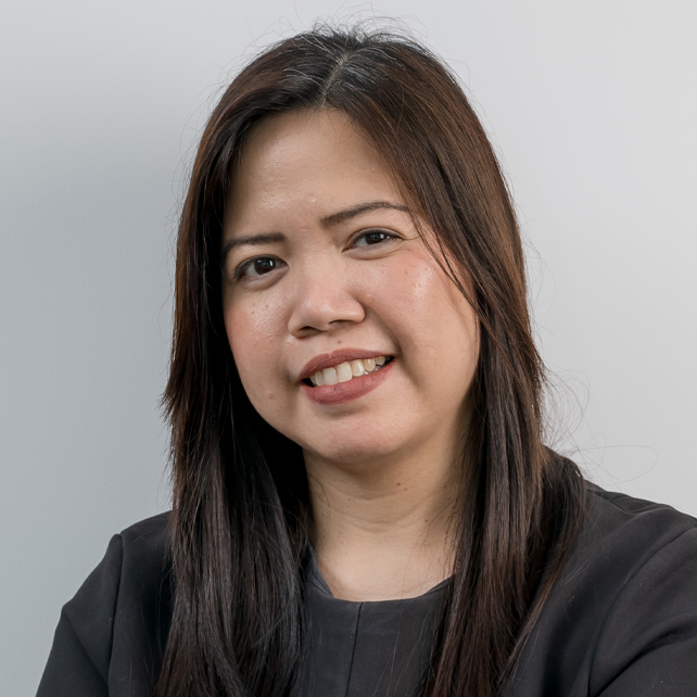 Portrait of a smiling woman with long dark hair wearing a black top against a gray background.