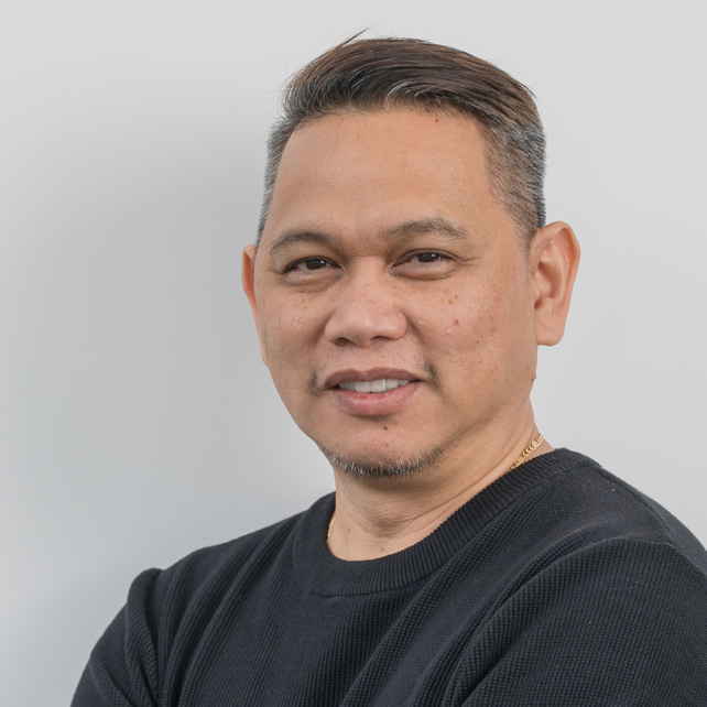 Portrait of a man with short hair wearing a black sweater, smiling slightly against a plain light gray background.