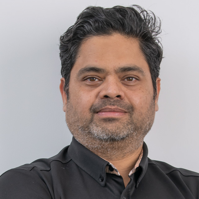 Portrait of a middle-aged man with dark, wavy hair and a trimmed beard wearing a black collared shirt.