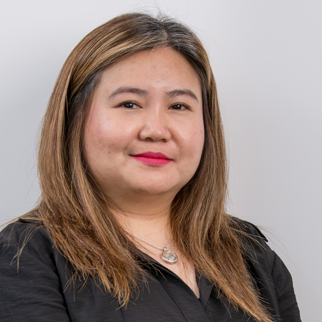 Portrait of a woman with long light brown hair, wearing a black top and a silver necklace, smiling slightly against a plain light background.