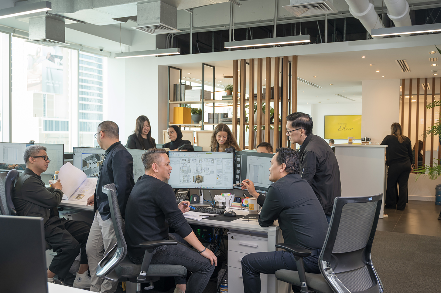Studio Eileen team collaborating around multiple computer monitors displaying interior design or architecture plans in a modern office space.