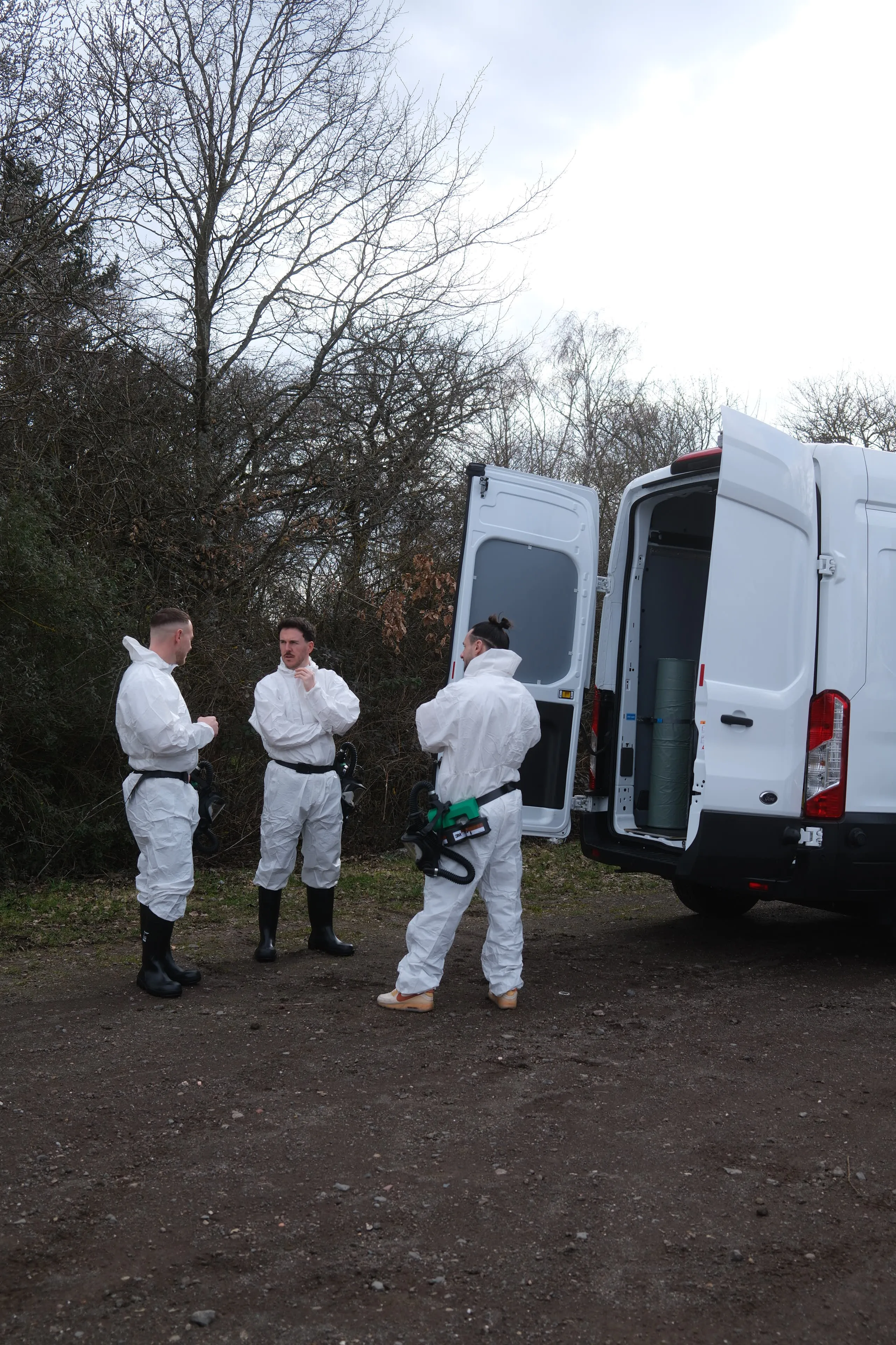 Team von Die Tatortreiniger Spezialisten in Schutzanzügen vor dem Einsatzfahrzeug. Zeigt wie sich Lennard, Dennis und Christian unterhalten.