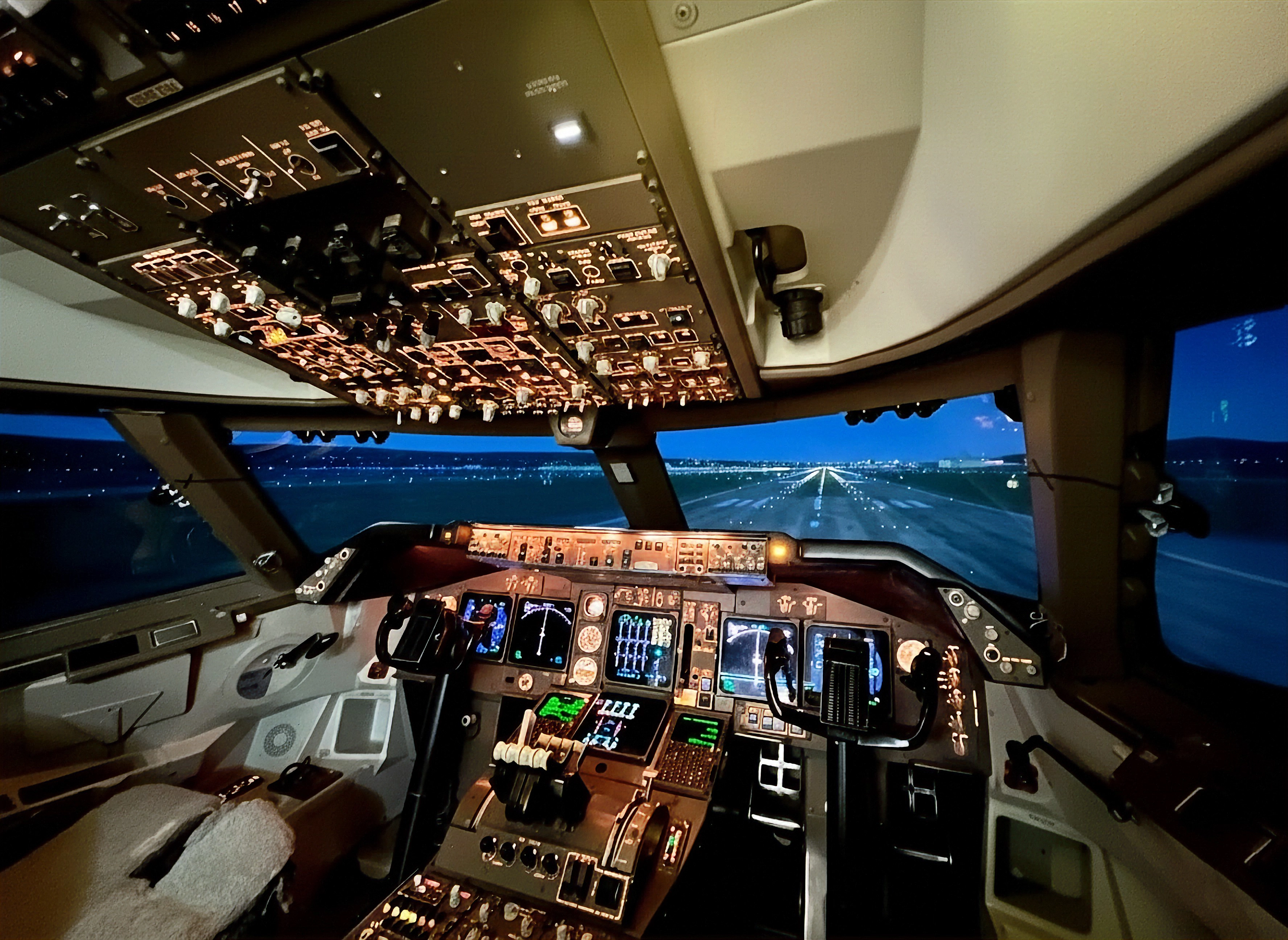 Illuminated airplane cockpit at night with runway visible through the front window.