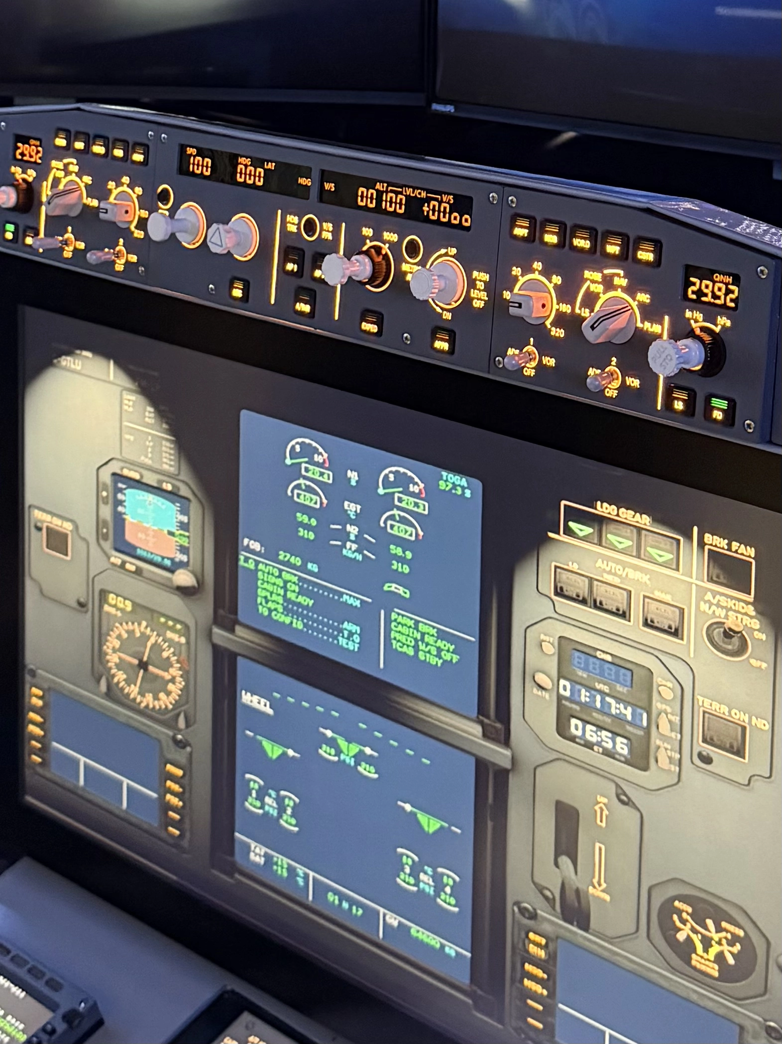 Close-up of an A320 flight simulator control panel showing multiple illuminated switches, dials, and digital screens with flight data and instruments.