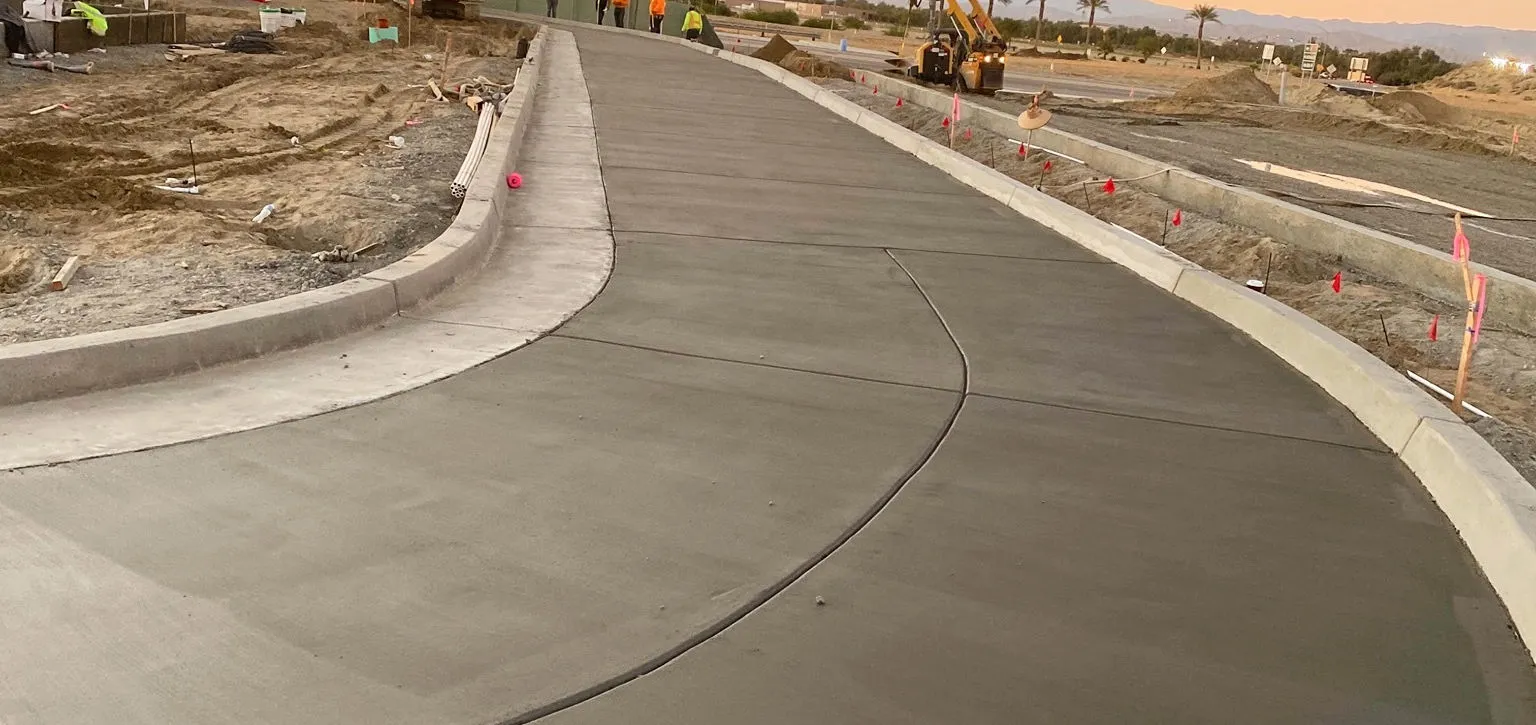 Newly poured curved concrete road with construction equipment and workers in the background.