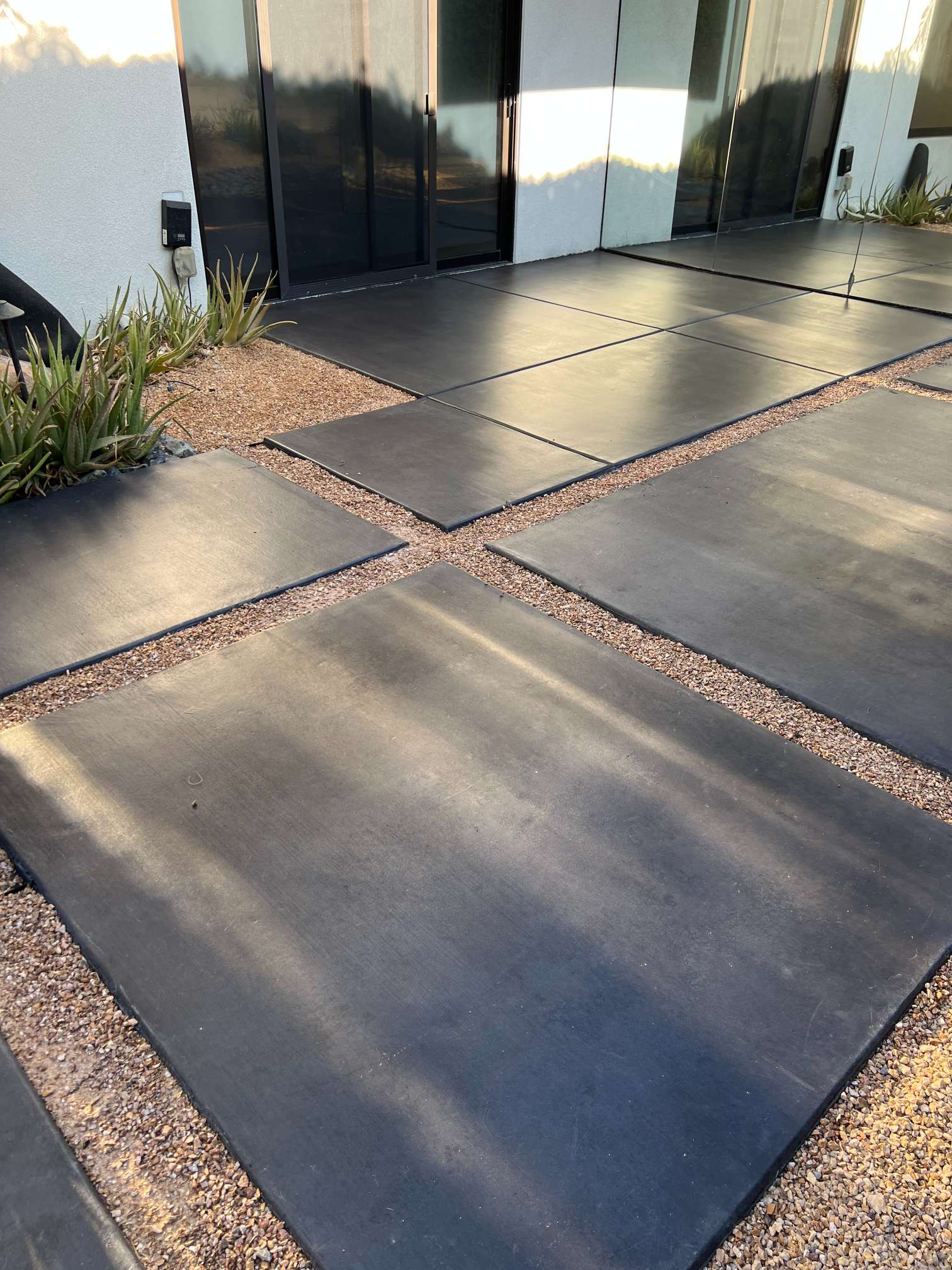 Modern outdoor patio with large dark square concrete pavers separated by small pebbles next to a glass door and succulents.