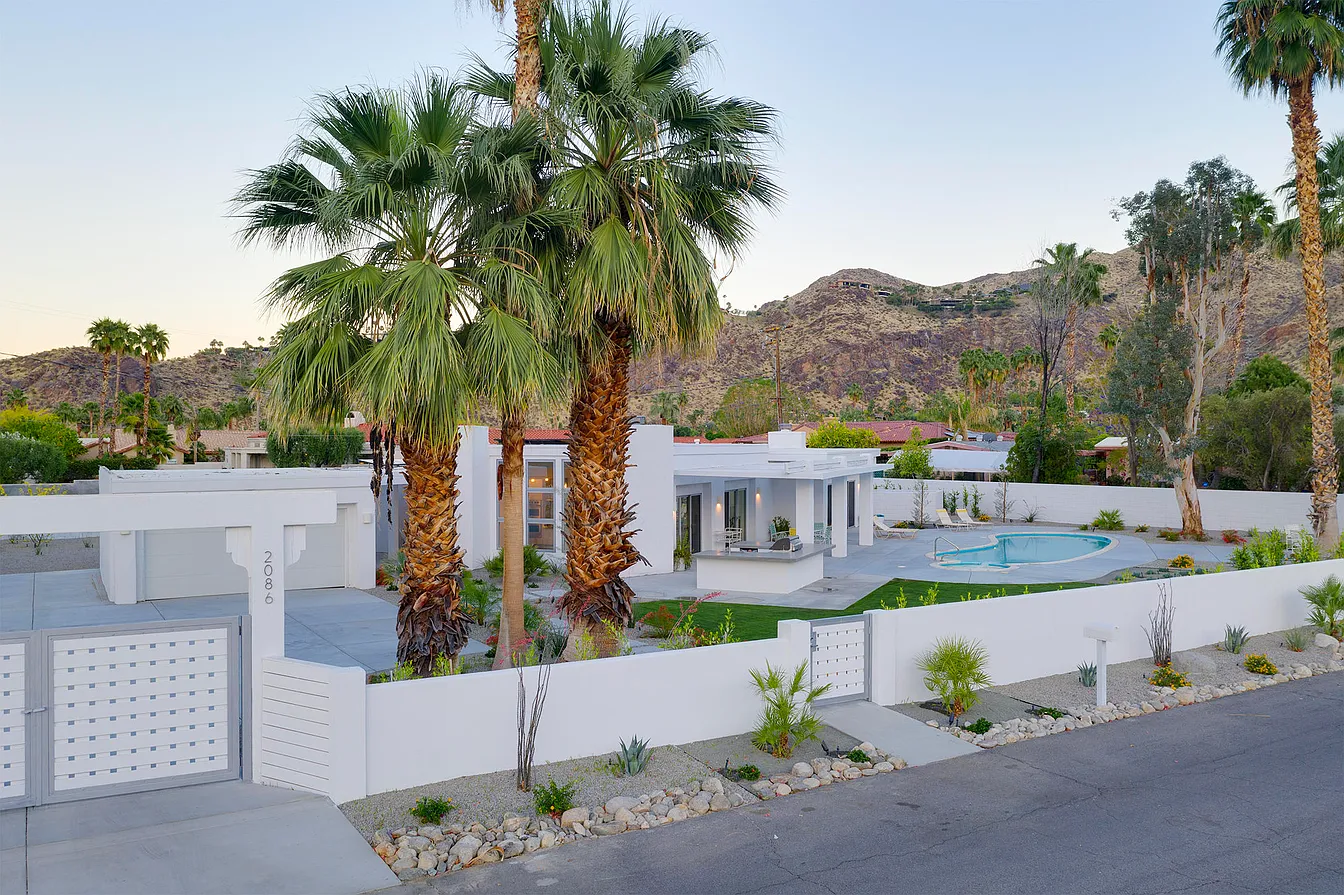 Modern white house with palm trees, a swimming pool, and a desert mountain background.