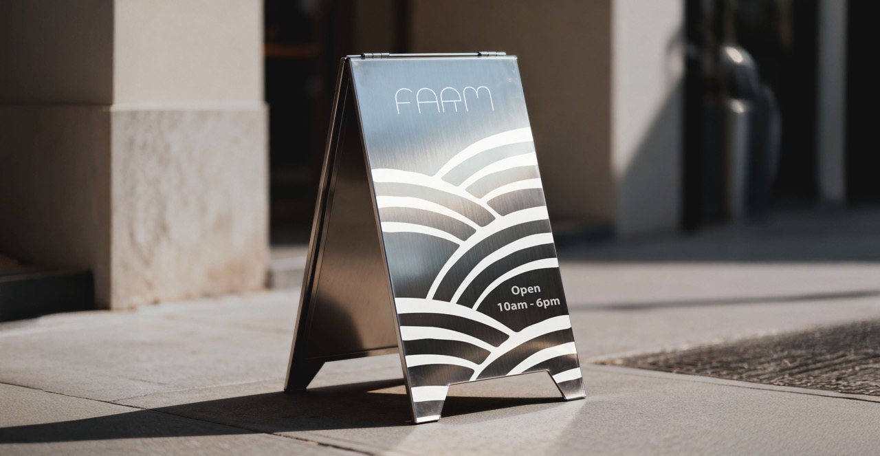 Metal street sign with the text 'FAAM' and 'Open 10am - 6pm' with white curved line designs on a sidewalk.