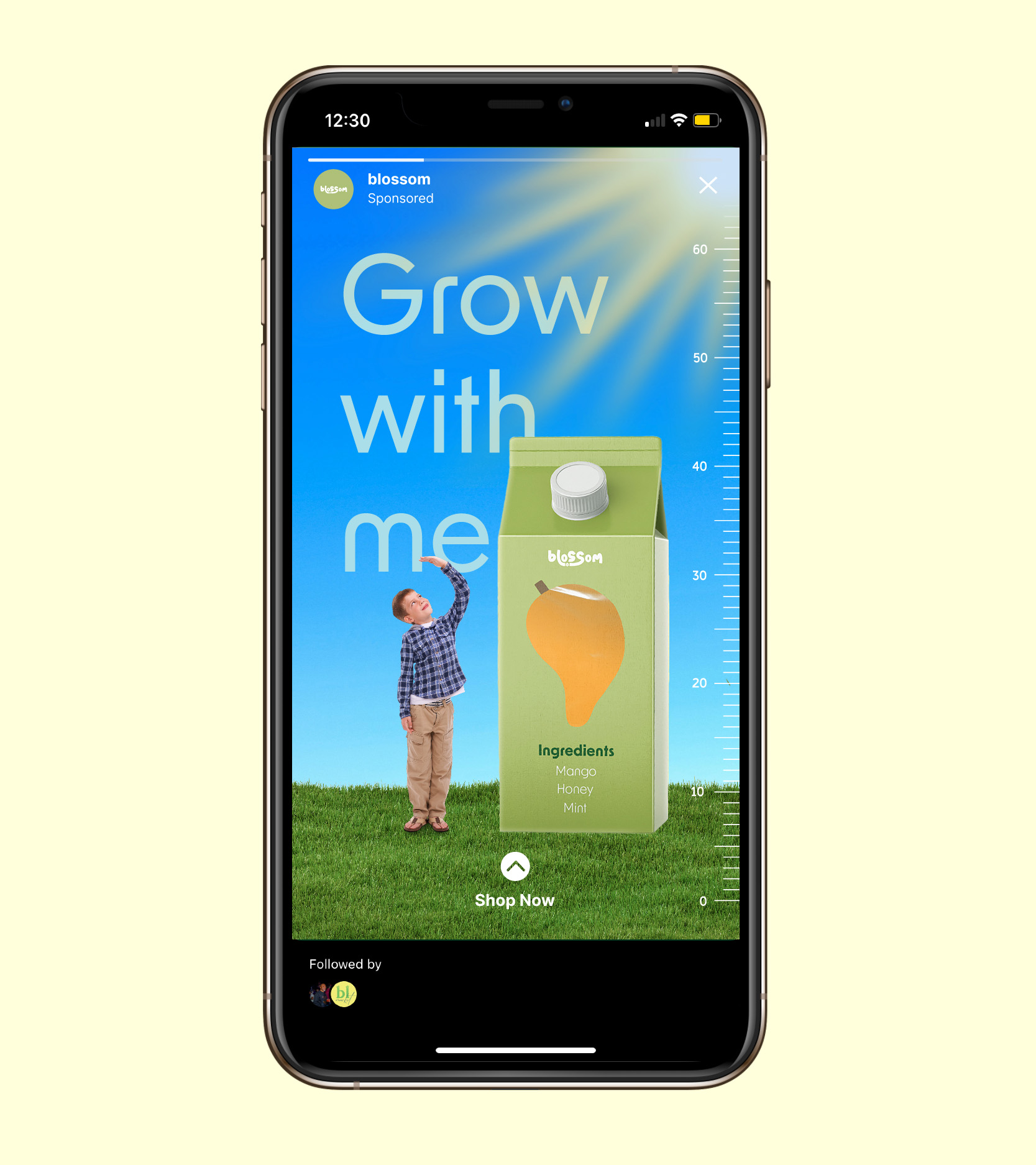 A boy standing on grass measuring his height with a blossom juice large carton with the text 'Grow with me.' 