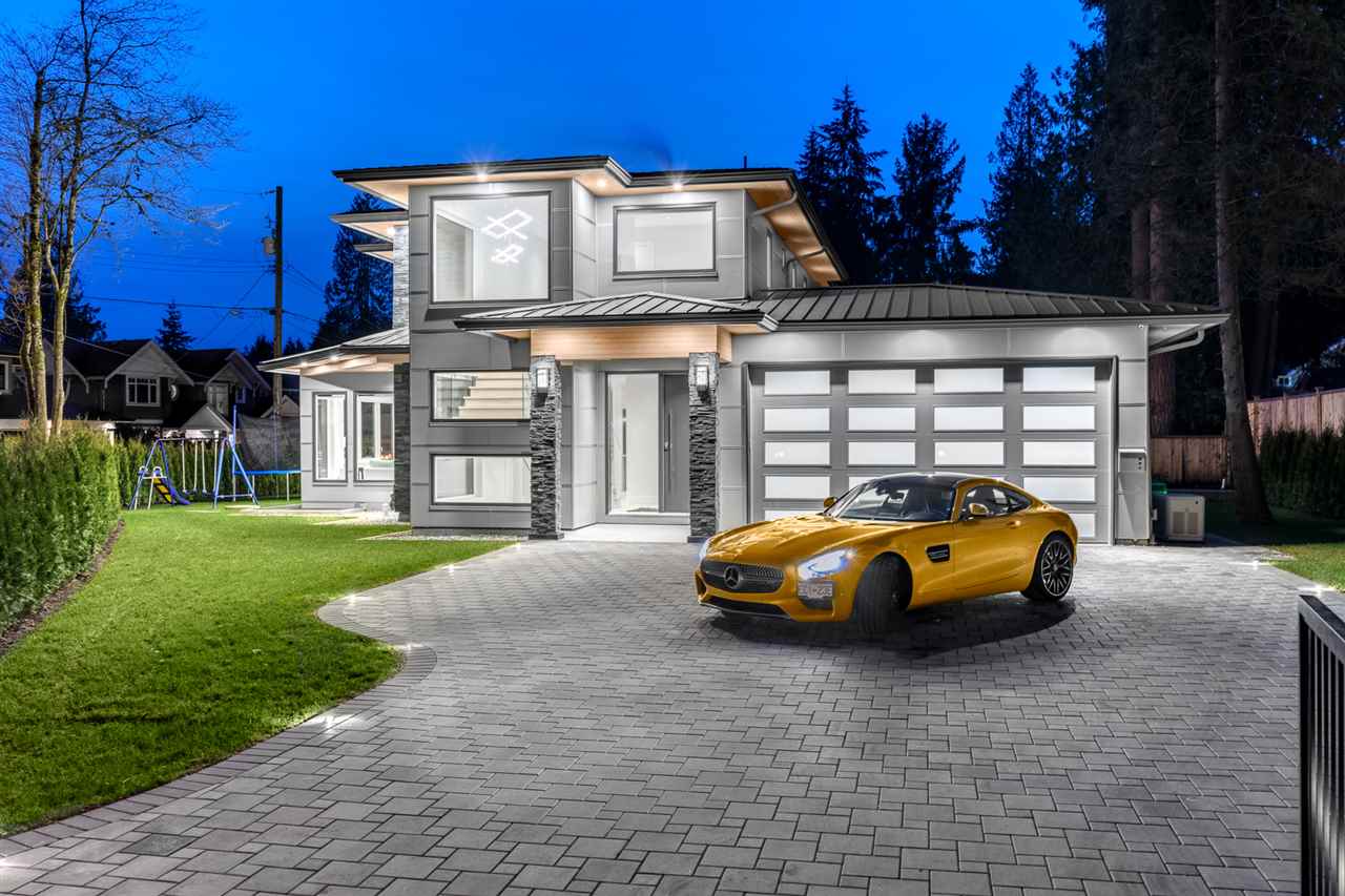 Modern two-story house with large windows, a neatly paved driveway, green lawn, and a yellow sports car parked in front at dusk.