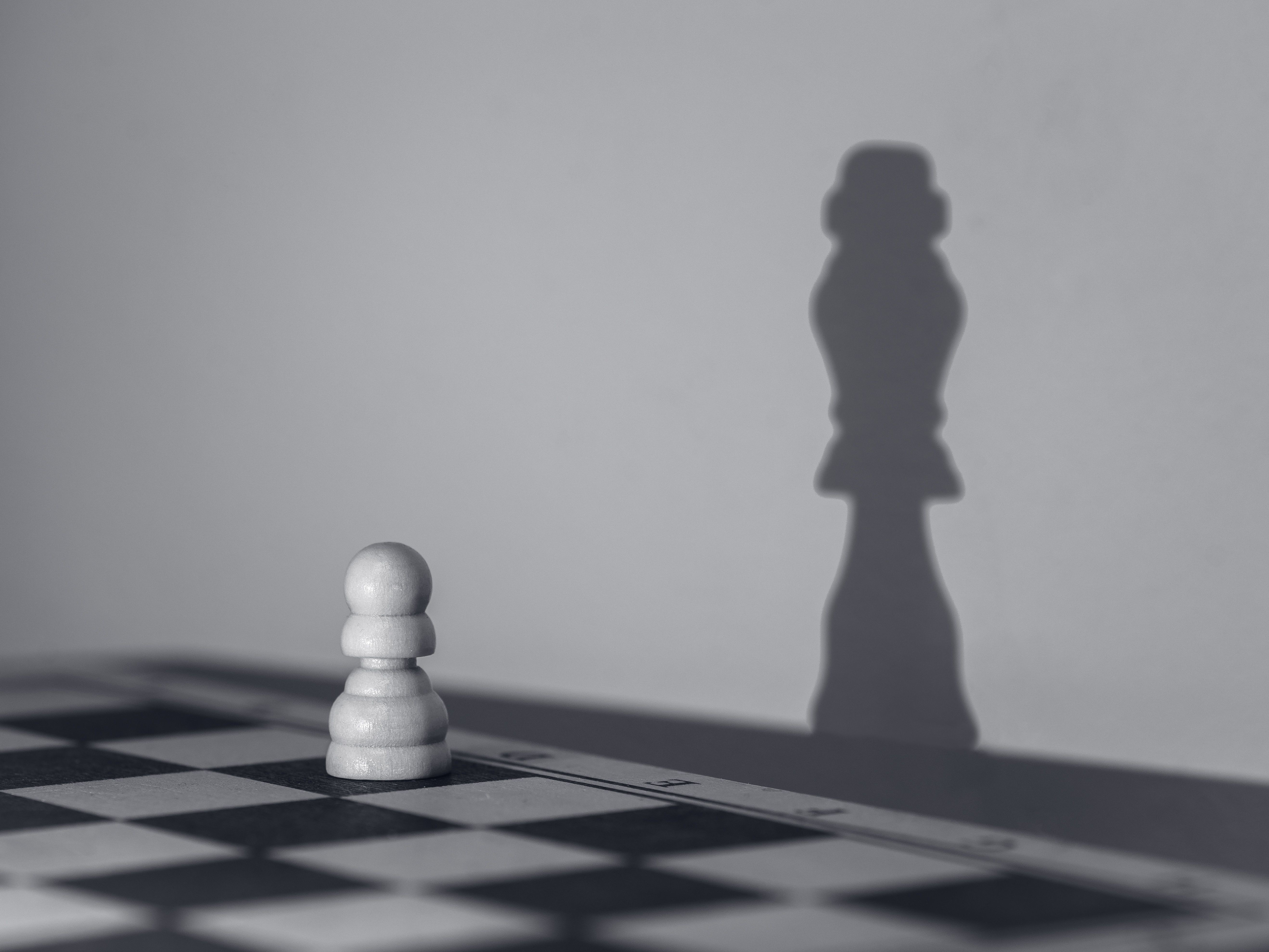 White chess pawn casting the shadow of a much more powerful chess piece, illustrating negotiating power and influence.