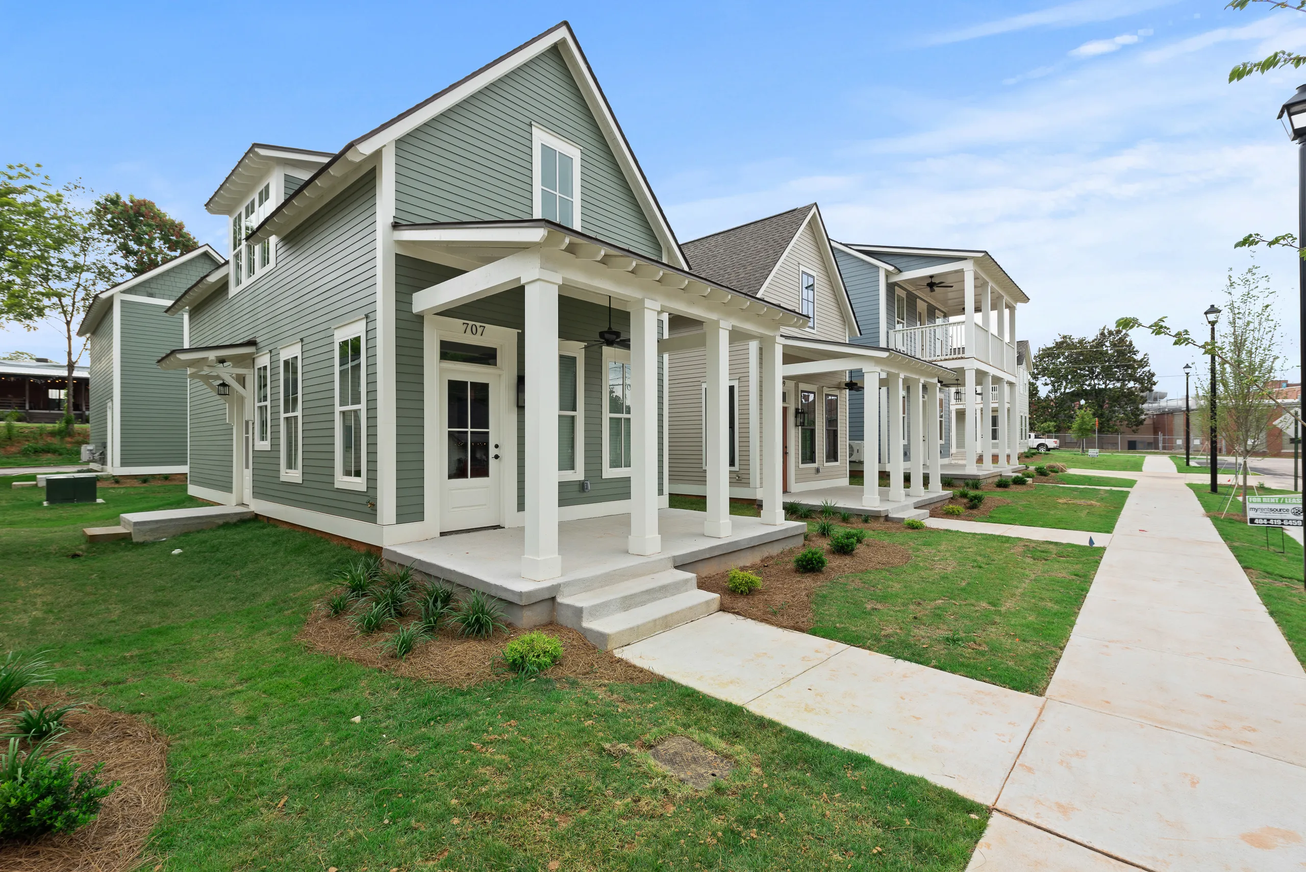 Single-story white house with gray roof, black window shutters, a well-maintained green lawn, and surrounding trees.